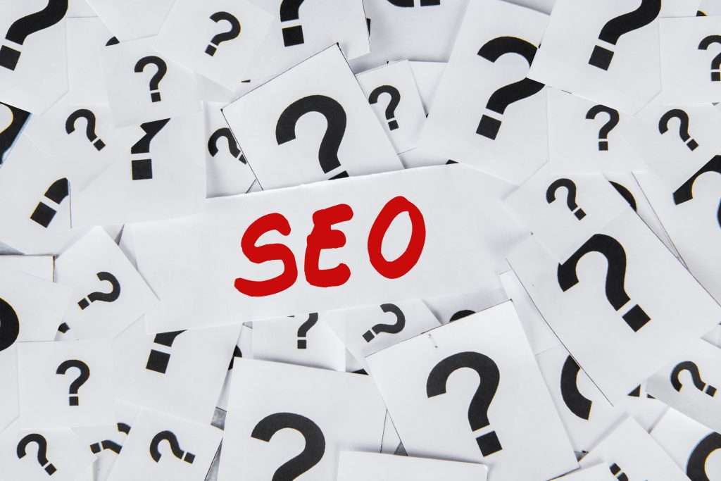 A pile of white cards with black question marks surrounds a central card that reads SEO in bold red letters, highlighting questions or confusion around SEO and its impact on platforms like Apple Maps.